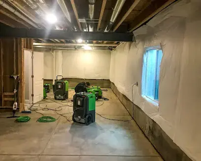 Dehumidifiers and air movers drying a basement with the lower drywall cut out