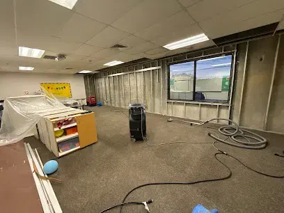 Dehumidifier and extension cords on the floor of an emptied commercial room mid dry-out