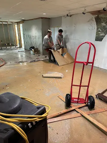 Two workers pulling up wet flooring in a basement room after water damage