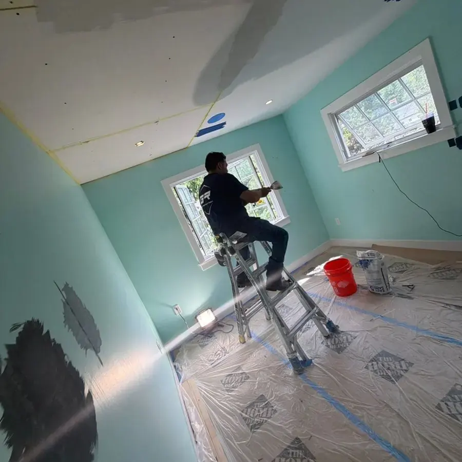 A worker on a ladder above plastic sheeting laid across the floor of a room under repair