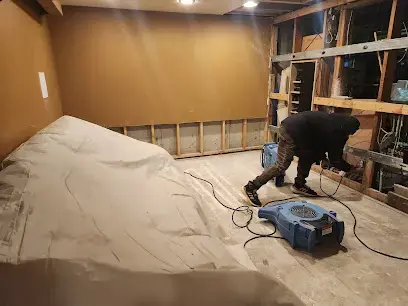 Technician setting an air mover in a Commerce City basement opened to the studs, with the floor covered in plastic